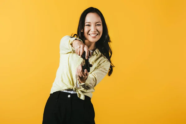 КИЕВ, УКРАИНА - 16 апреля 2019 года: улыбающаяся азиатка, играющая в видеоигру с джойстиком, изолированная на желтом — стоковое фото