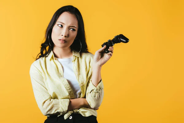 KYIV, UCRANIA - 16 DE ABRIL DE 2019: atractiva chica asiática sosteniendo joystick, aislada en amarillo - foto de stock