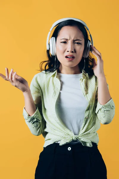 Confused asian girl listening music with headphones, isolated on yellow — Stock Photo