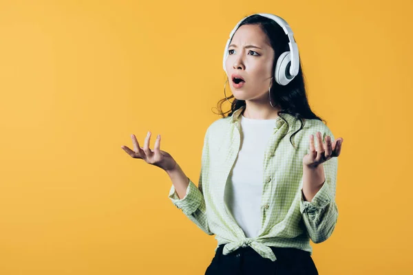 Frustrado asiático chica escuchando música con auriculares, aislado en amarillo - foto de stock