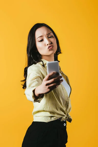 Beautiful asian girl taking selfie on smartphone isolated on yellow — Stock Photo