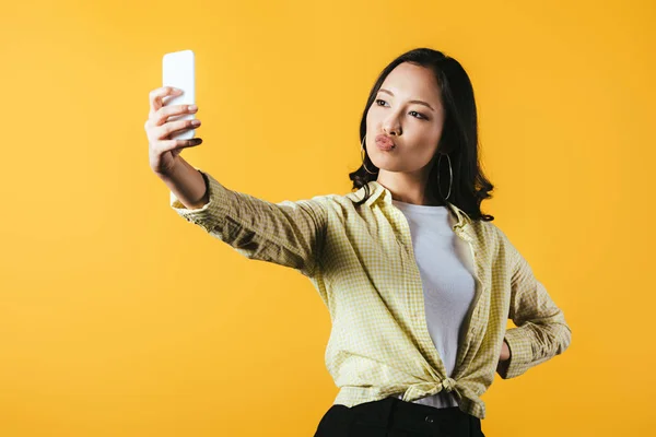 Attractive asian girl taking selfie on smartphone isolated on yellow — Stock Photo