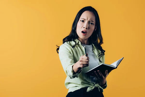 Irritado asiático mulher com notebook e caneta, isolado no amarelo — Fotografia de Stock