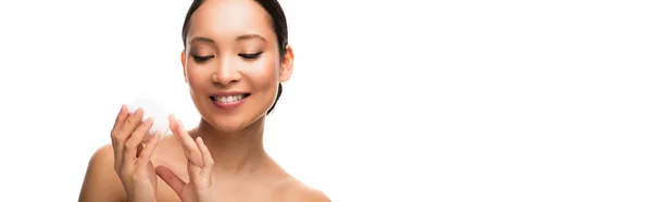 Усміхнена азіатська жінка тримає крем для обличчя, ізольована на білому — стокове фото