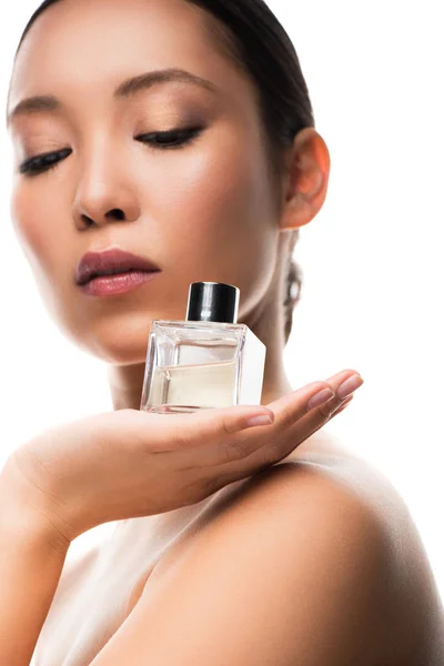 Tierna chica asiática con los ojos cerrados celebración de la botella de perfume, aislado en blanco - foto de stock