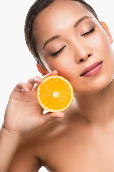 Hermosa mujer asiática tierna con los ojos cerrados sosteniendo naranja, aislado en blanco - foto de stock