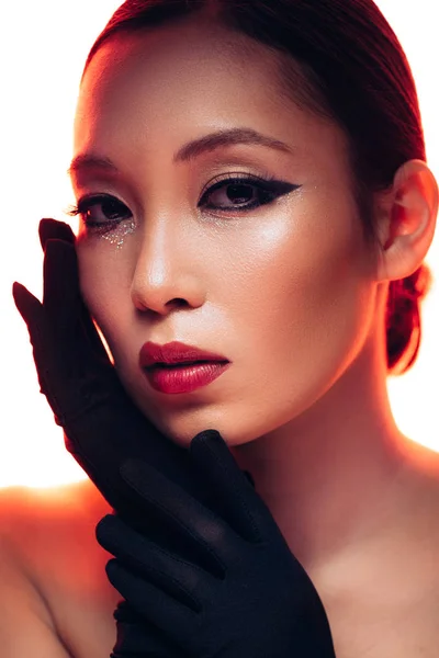 Mujer asiática en guantes negros con maquillaje en luz roja, aislado en blanco - foto de stock