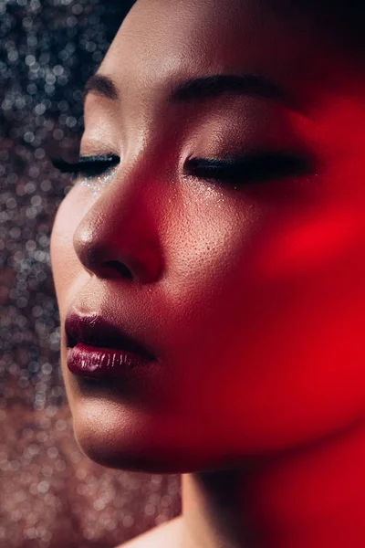 Close up of sensual asian girl with makeup on closed eyes in red light — Stock Photo