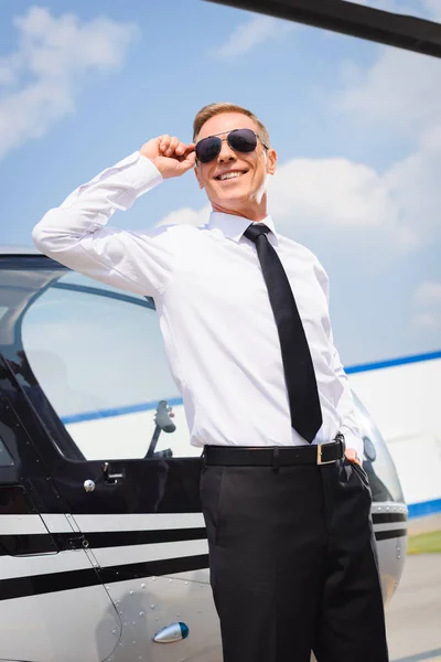 Lächelnder Pilot in offizieller Kleidung mit Sonnenbrille in der Nähe des Hubschraubers — Stockfoto