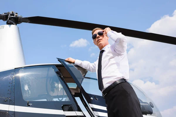 Vista a basso angolo di Pilot in abbigliamento formale e occhiali da sole vicino all'elicottero — Foto stock