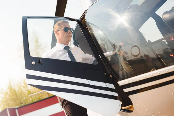 Beau pilote en tenue formelle et lunettes de soleil ouvrant la porte de l'hélicoptère — Photo de stock