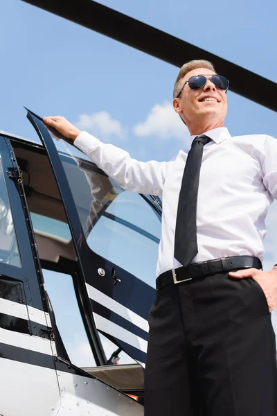 Piloto sonriente en ropa formal y gafas de sol abriendo la puerta del helicóptero - foto de stock