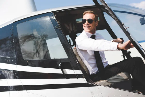 Gutaussehender Pilot in offizieller Kleidung und Sonnenbrille sitzt in Helikopterkabine — Stockfoto