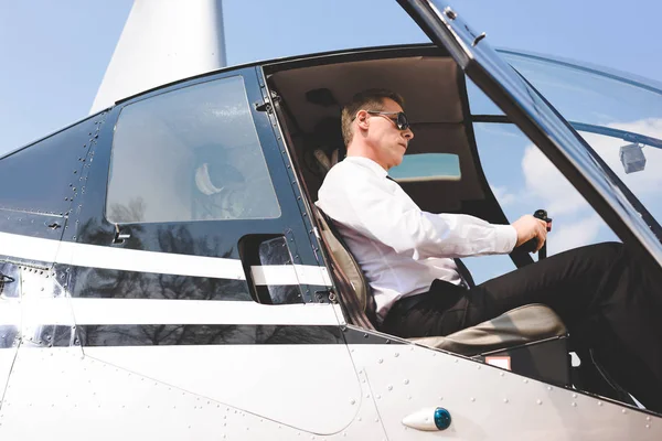 Gut aussehender Pilot mit Sonnenbrille und formeller Kleidung sitzt in der Helikopterkabine — Stockfoto