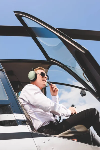 Low angle view of Pilot in sunglasses and headset sitting in helicopter cabin — Stock Photo