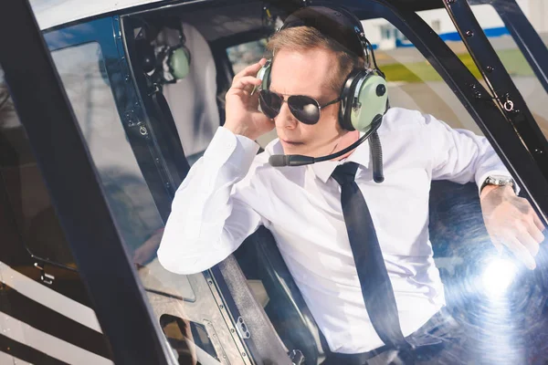 Pilote en lunettes de soleil et casque avec microphone assis dans la cabine de l'hélicoptère — Photo de stock