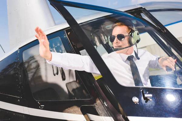 Piloto en gafas de sol y auriculares sentado en cabina de helicóptero y mostrando señal de stop - foto de stock