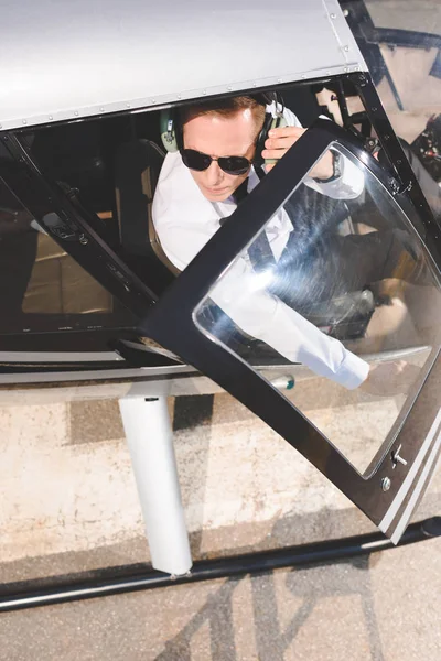 Vista superior de Piloto en gafas de sol y auriculares sentado en cabina de helicóptero - foto de stock