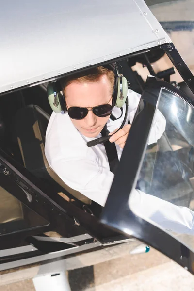 Vista superior de Piloto en gafas de sol y auriculares con micrófono sentado en cabina de helicóptero - foto de stock