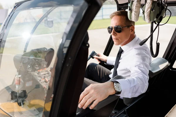 Beau pilote en lunettes de soleil assis dans la cabine de l'hélicoptère — Photo de stock