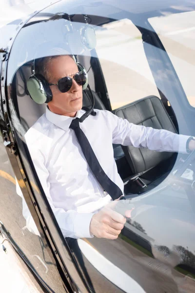 Reifer Pilot in offizieller Kleidung und Kopfhörer sitzt in Helikopterkabine — Stockfoto