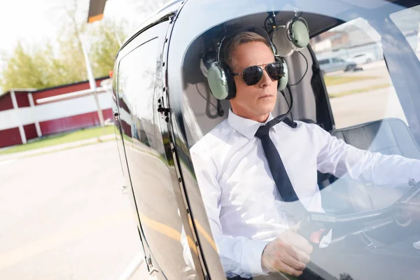 Reifer Pilot in offizieller Kleidung und Kopfhörer sitzt in Helikopterkabine — Stockfoto
