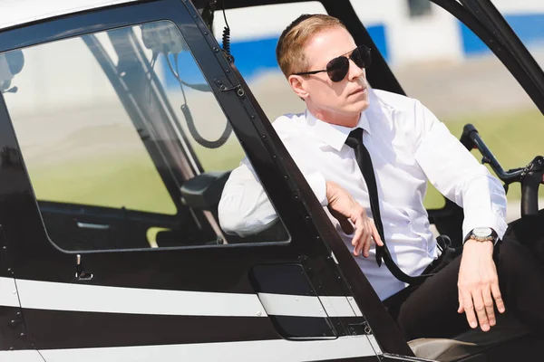 Серйозний зрілий пілот у формальному носінні сидить у вертольоті кабіни — стокове фото