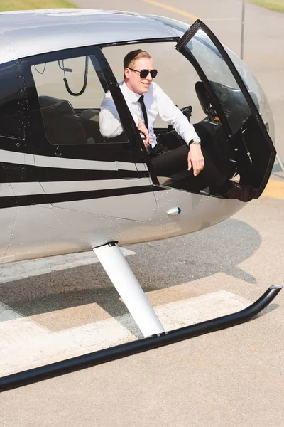 Mature Pilot in formal wear smiling and sitting in helicopter cabin — Stock Photo