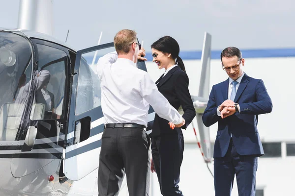 Empresarios en ropa formal cerca de helicóptero y piloto - foto de stock