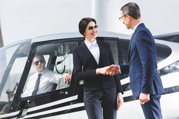Uomini d'affari in giacca e cravatta stretta di mano vicino elicottero con pilota — Foto stock