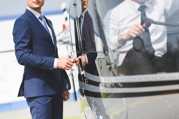 Vue recadrée du pilote assis en hélicoptère pendant que l'homme d'affaires ouvre la porte — Photo de stock