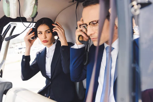 Mujer de negocios y hombre de negocios en auriculares sentados en cabina de helicóptero - foto de stock