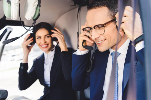 Smiling businesswoman and businessman in headsets sitting in helicopter cabin — Stock Photo