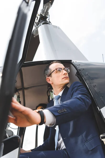 Vista de bajo ángulo del hombre de negocios en desgaste formal sentado en cabina de helicóptero - foto de stock