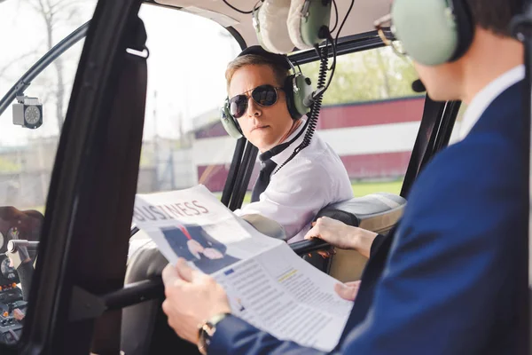 Pilot in headset and businessman with newspaper in helicopter cabin — Stock Photo