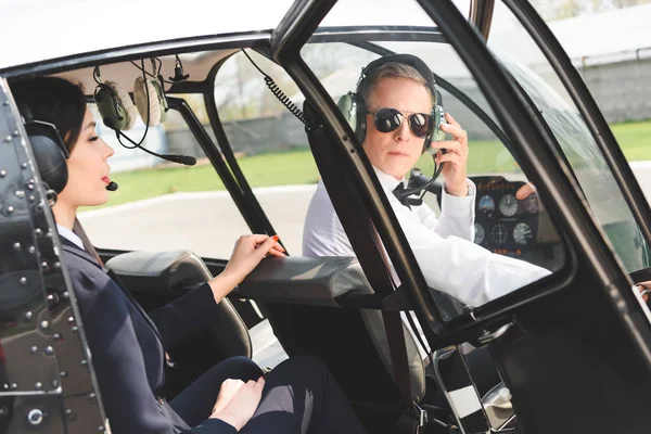 Femme d'affaires et pilote dans des casques assis dans la cabine de l'hélicoptère — Photo de stock