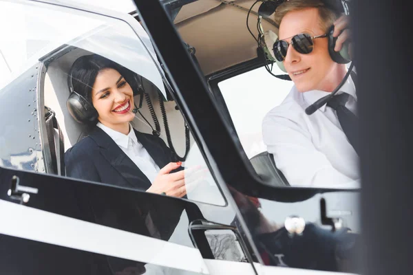 Donna d'affari sorridente e pilota in cuffia seduto in cabina elicottero — Foto stock