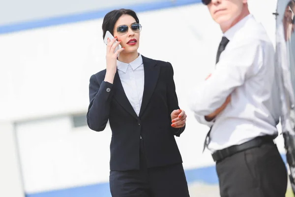 Избирательный фокус деловой женщины, говорящей на смартфоне рядом с мужчиной — стоковое фото