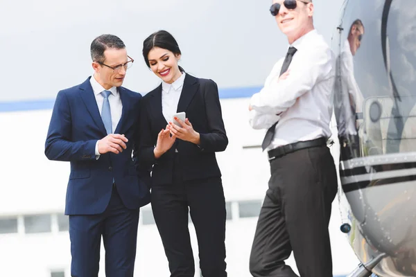 Empresários usando smartphone perto piloto e helicóptero — Fotografia de Stock