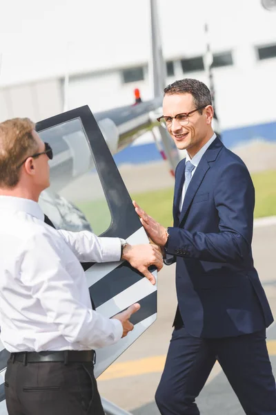 Pilot in formal wear near businessman opening door of helicopter — Stock Photo