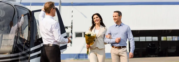 Panoramaaufnahme glücklicher Eheleute bei romantischem Date in der Nähe von Hubschrauber und Pilot — Stockfoto