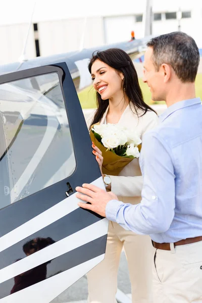 Husband and wife with flowers on romantic date opening door of helicopter — Stock Photo