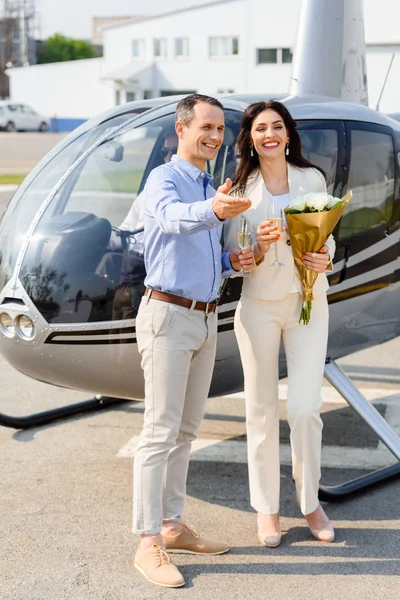 Happy husband and wife with flowers on romantic date near helicopter — Stock Photo