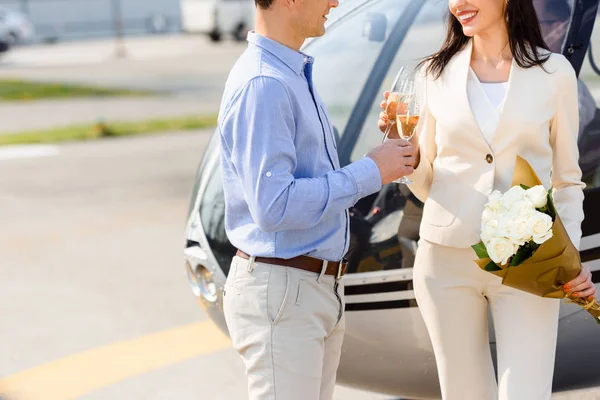 Cropped view of husband and wife clinking champagne glasses on romantic date near helicopter — Stock Photo