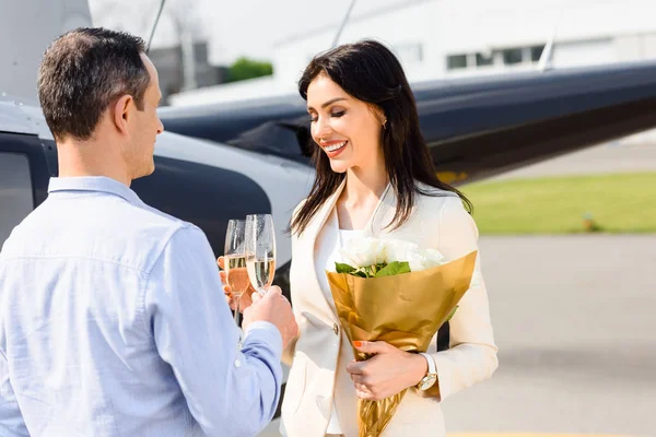 Husband and wife clinking champagne glasses on romantic date near helicopter — Stock Photo