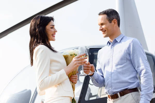 Husband and wife clinking champagne glasses on romantic date near helicopter — Stock Photo