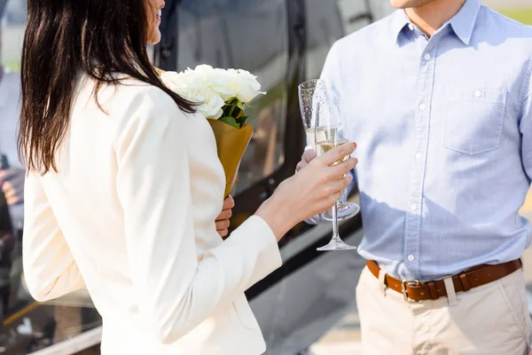 Cropped view of husband and wife with champagne glasses and flowers on romantic date — Stock Photo