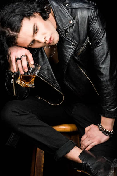 Hombre triste sentado en la silla y sosteniendo vaso de whisky aislado en negro - foto de stock