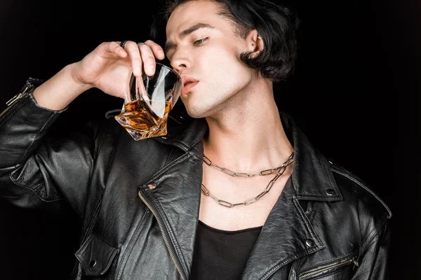 Homem bonito em jaqueta de couro beber uísque isolado em preto — Fotografia de Stock