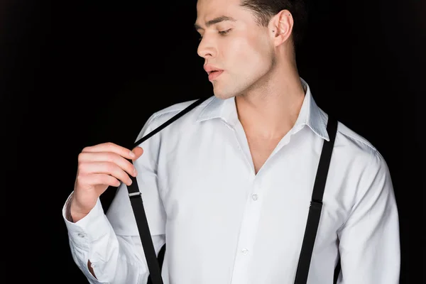 Young man in white shirt touching suspenders isolated on black — Stock Photo